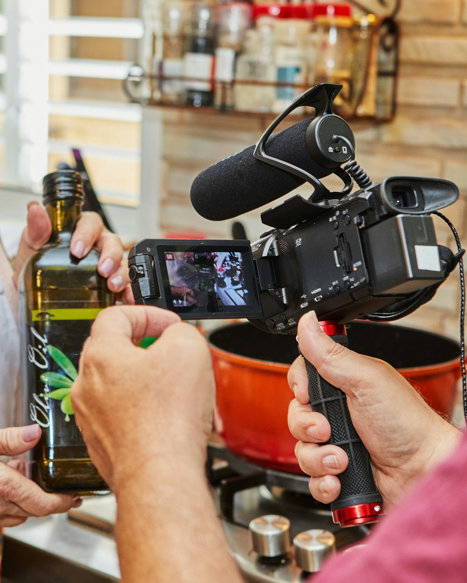 They are filming video of cooking, bottle of olive oil in the hands of the cook